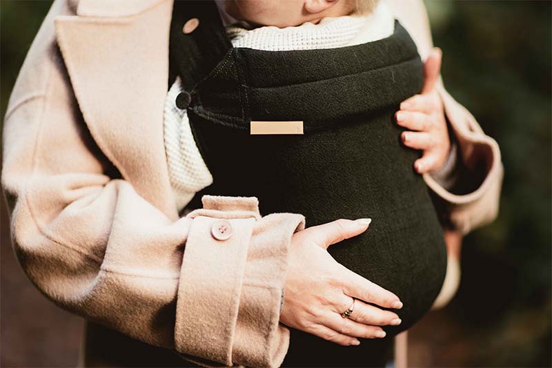 Beauden The Label deep green baby carrier modelled with trench coat Beauden the Label